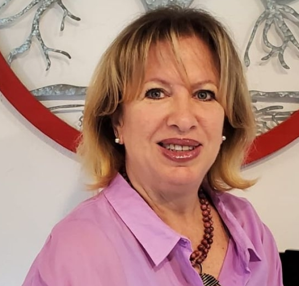 Portrait of Valeria Starowlansky, a smiling woman with blonde hair, wearing a pink blouse and beaded necklace