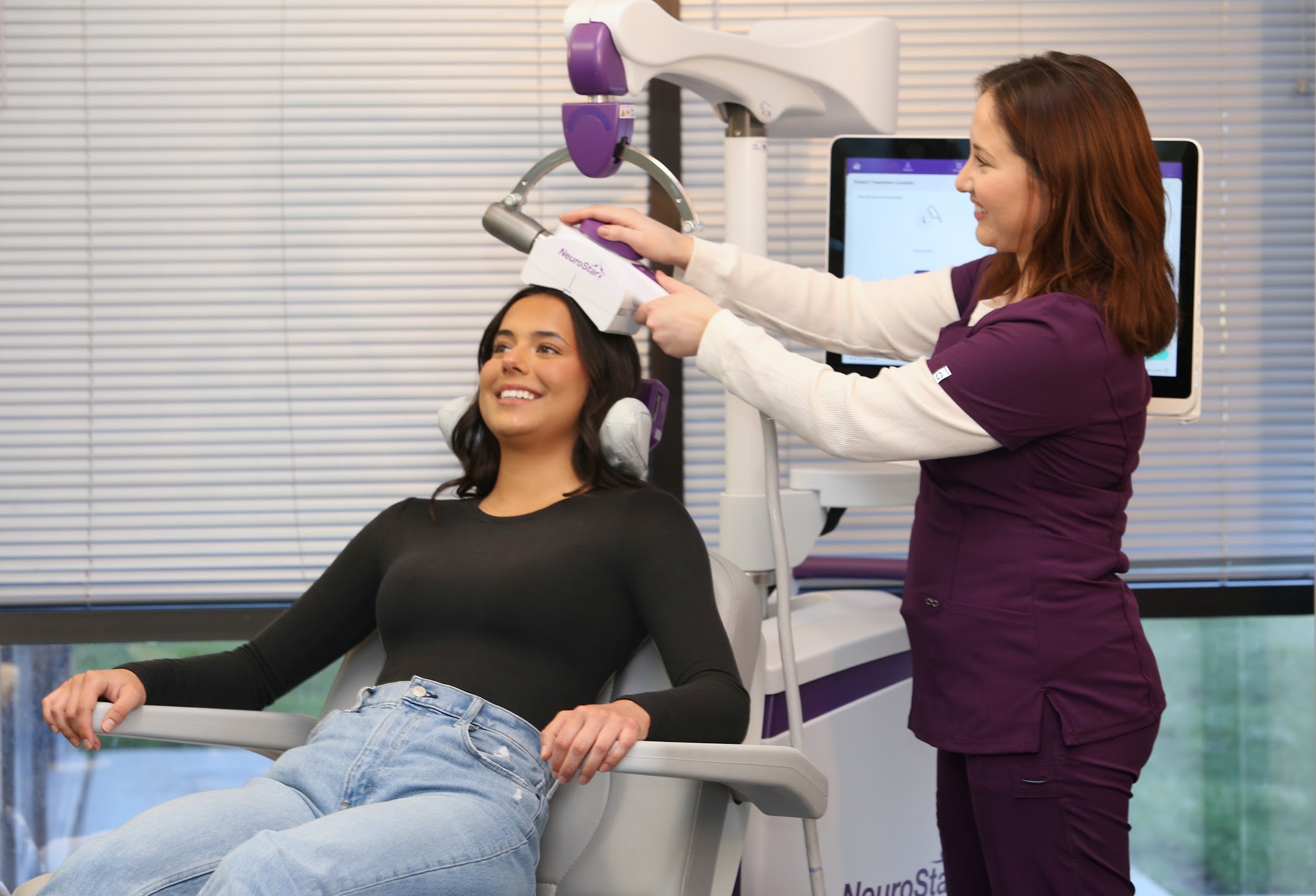 Una paciente sonriente que recibe un tratamiento con NeuroStar TMS mientras el profesional ajusta el dispositivo