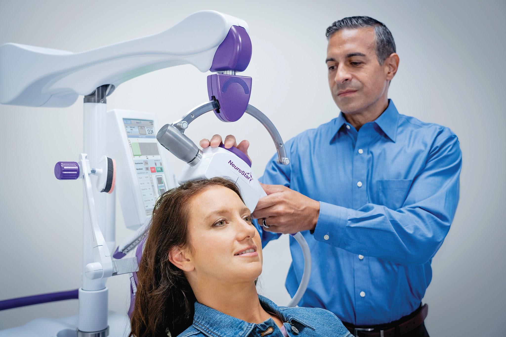 Doctor carefully positioning a magnetic therapy coil on a patient's head in a clinic room.